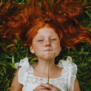 Meisje met rood haar en sproeten in het gras. Rood haar en sproeten gaan samen omdat beide uit hetzelfde stukje DNA komen